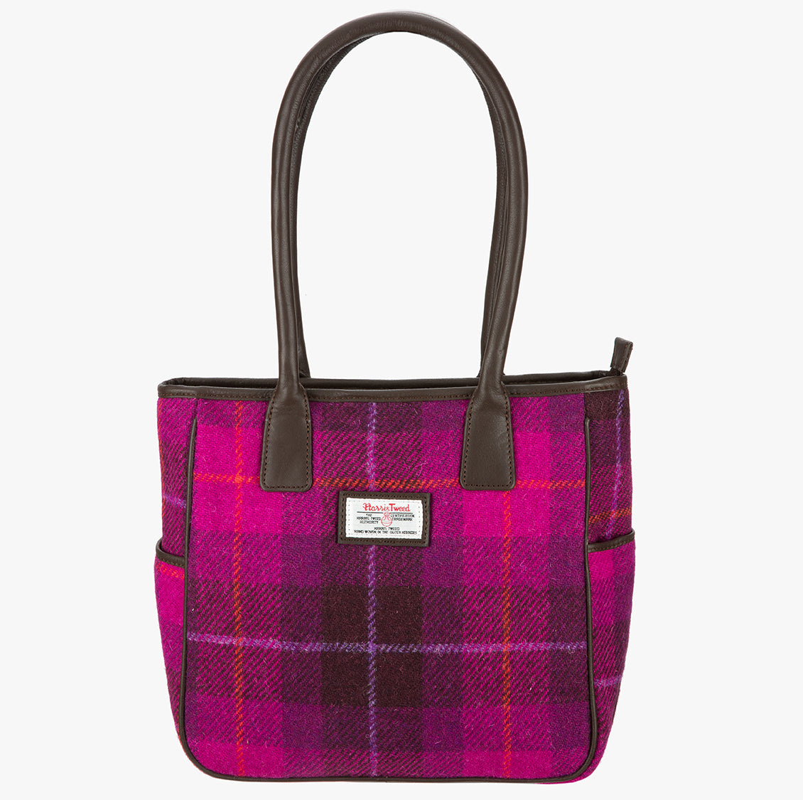 Harris Tweed tote bag in a cerise check with brown leather handles that go over the shoulder.  It has a pocket on each side of the bag trimmed with brown leather. It also has a harris tweed logo on the front of the bag in the middle which is sewn onto a leather label holder.