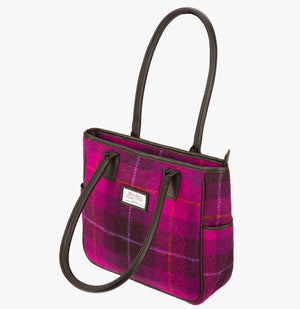 Harris Tweed tote bag with handles that go over the shoulder, it is a bright pink and dark pink check. This bag is cerise Harris Tweed with brown leather handles. It has a pocket on each side of the bag trimmed with navy leather. This bag has the front folded over.