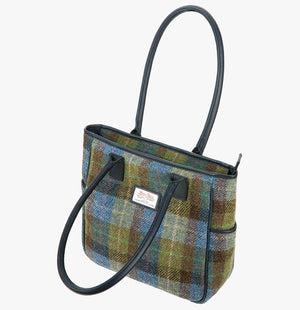 Harris Tweed tote bag with handles that go over the shoulder, it is a blue, green, and brown check. This bag is denim/sage Harris Tweed with navy blue leather handles. It has a pocket on each side of the bag trimmed with navy leather. This bag has the front folded over.