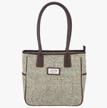 Harris Tweed tote bag in a pastel check with brown leather handles that go over the shoulder. The colour is a brown and cream herringbone with a pink and pale blue overcheck. It has a pocket on each side of the bag trimmed with brown leather. It also has a harris tweed logo on the front of the bag in the middle which is sewn onto a leather label holder.