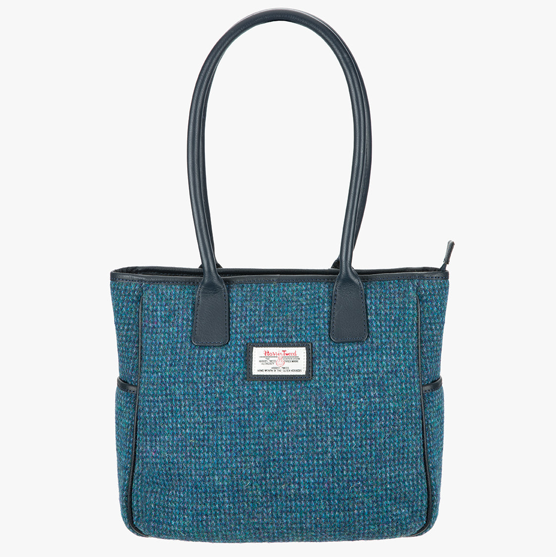 Harris Tweed tote bag in teal, it has a black leather handles that go over the shoulder.  It has pockets on each side of the bag and a Harris Tweed logo on the front.