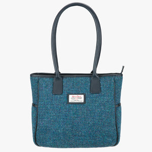 Harris Tweed tote bag in teal, it has a black leather handles that go over the shoulder.  It has pockets on each side of the bag and a Harris Tweed logo on the front.