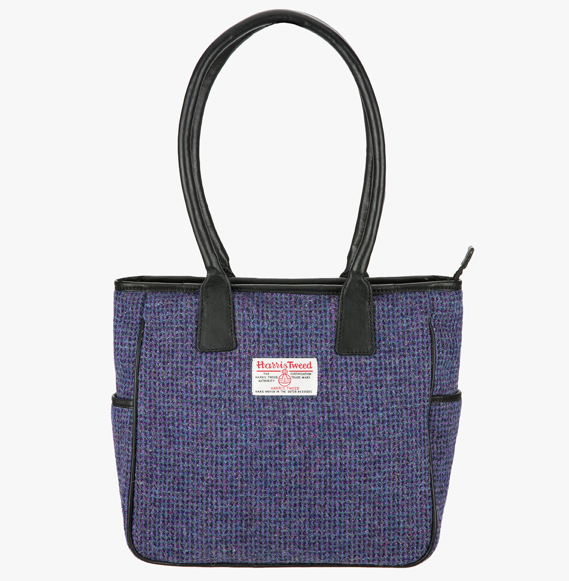 Harris Tweed tote bag with handles that go over the shoulder. This bag is violet Harris Tweed with black leather handles. It has a pocket on each side of the bag trimmed in black leather and a harris tweed logo on the front in the middle of the bag.