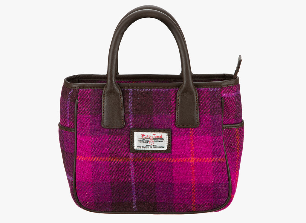 Harris Tweed hand held bag in a cerise check with brown leather handles. The colour is a bright pink and dark pink check. It has a pocket on each side of the bag trimmed with brown leather. It also has a Harris Tweed logo on the front of the bag in the middle which is sewn onto a leather label holder.