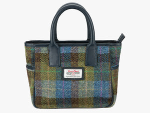 Harris Tweed handheld bag in denim check with navy leather handles. The colour is a blue, green and brown check . It has a pocket on each side of the bag trimmed with navy leather. It also has a Harris Tweed logo on the front of the bag in the middle which is sewn onto a leather label holder.