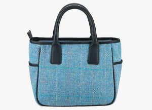 This is the reverse of the Harris Tweed handheld bag in sky. The colour is sky blue with a turquoise, pink and white overcheck. It has a pocket on each side of the bag trimmed with navy leather. It also has short navy blue leather handles.