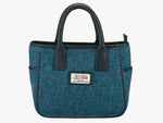 Harris Tweed handheld bag in teal check with black leather handles. It has a pocket on each side of the bag trimmed with black leather. It also has a Harris Tweed logo on the front of the bag in the middle which is sewn onto a leather label holder.
