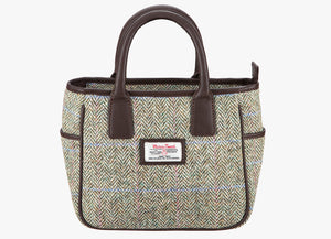 Harris Tweed handheld bag in pastel with brown leather handles. The colour is a cream and brown herringbone with a pink and blue overcheck . It has a pocket on each side of the bag trimmed with brown leather. It also has a Harris Tweed logo on the front of the bag in the middle which is sewn onto a leather label holder.