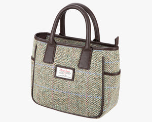 This is a three-quarters view of the Harris Tweed handheld bag. The colour is a cream and brown herringbone with a pink and blue overcheck . It has a pocket on each side of the bag trimmed with brown leather. It also has short brown leather handles.
