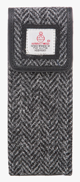 Front view of the Harris Tweed glasses case in charcoal herringbone, it is a charcaol and black small herringbone design and is trimmed in black leather. This is a rectangular Harris Tweed glasses case with a magnetic closure at the top and a small square Harris tweed logo on the front trimmed with leather.