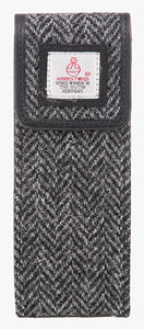 Front view of the Harris Tweed glasses case in charcoal herringbone, it is a charcaol and black small herringbone design and is trimmed in black leather. This is a rectangular Harris Tweed glasses case with a magnetic closure at the top and a small square Harris tweed logo on the front trimmed with leather.