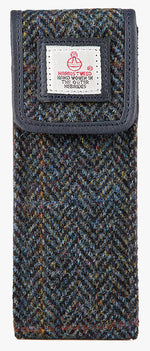 Front view of the Harris Tweed glasses case in midnight blue, it is a navy and black small herringbone design with an overcheck in brown and a fine orange. This case is trimmed in navy leather. This is a rectangular Harris Tweed glasses case with a magnetic closure at the top and a small square Harris tweed logo on the front trimmed with leather.