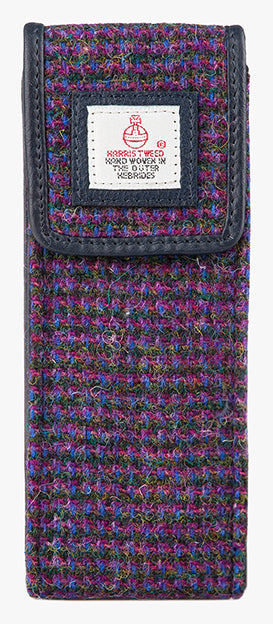 This is the front of the Harris Tweed glasses case in violet, it is a purple, black, pink and blue subtle check design and is trimmed in black leather. This is a rectangular Harris Tweed glasses case with a magnetic closure at the top and a small square Harris tweed logo on the front trimmed with leather.