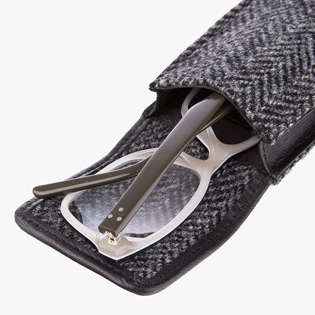 Harris Tweed glasses case in charcoal herringbone, it is a charcaol and black small herringbone design and is trimmed in black leather. This photo shows the glassses case in use, it is a shot of the open case and a pair of glasses half way pulled out of the case to demostrate usage.