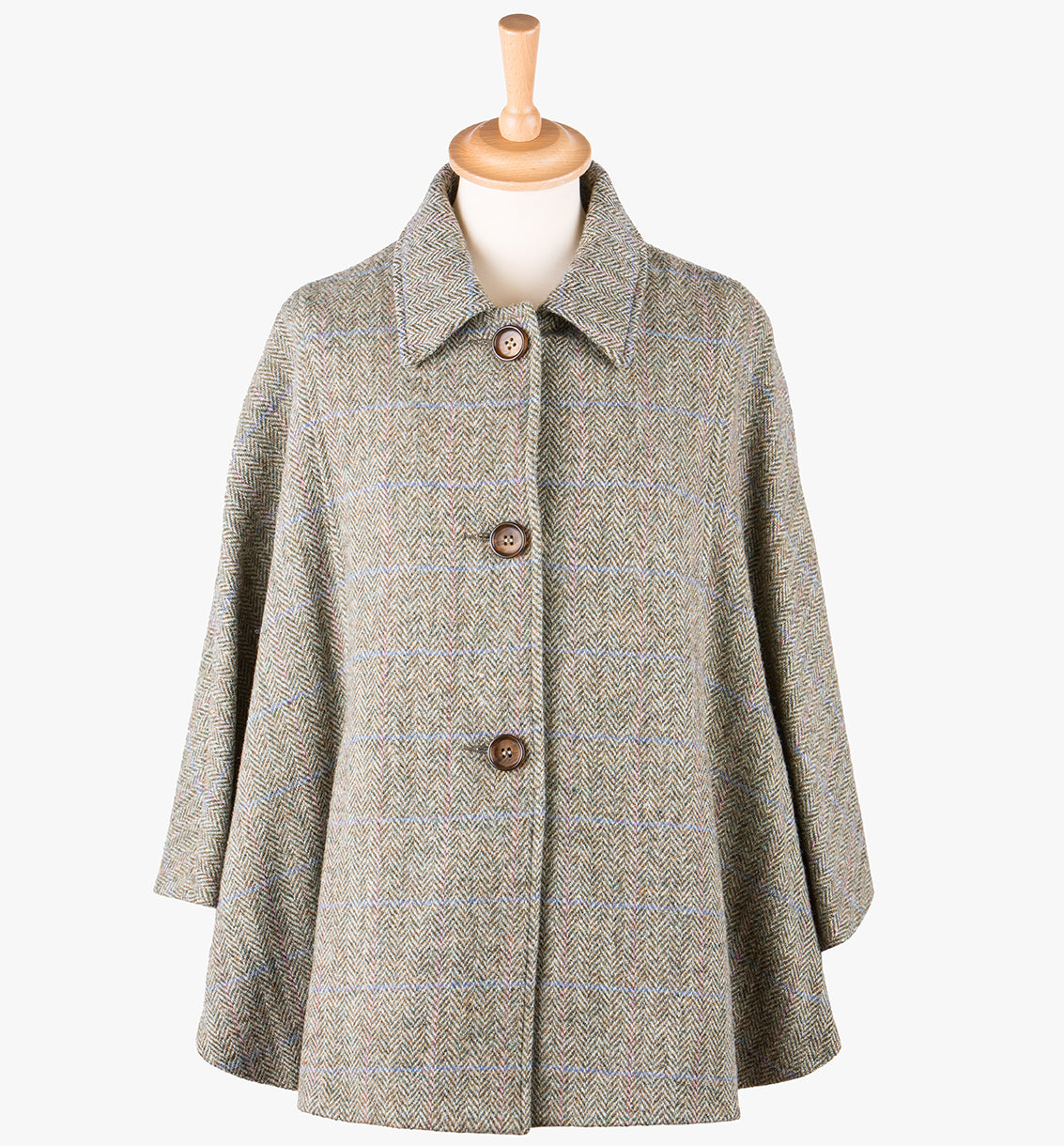 This is the Harris Tweed cape in Pastel check,  the colour is a beige and cream small herringbone with a blue and pink overcheck. It has 3 buttons and a collar which can be worn both up and down. It has buttons at the side which hold the cape together to give it more structure. This cape has two pockets and is a one size fits all garment.