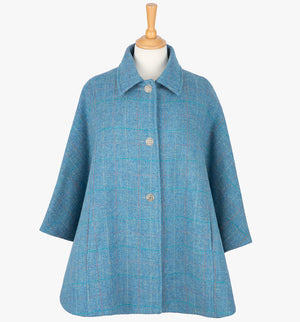 This is the Harris Tweed cape in sky blue, the colour is sky blue with a white, red and subtle turquoise overcheck. It has 3 buttons and a collar that can be worn both up and down. It has buttons at the side which hold the cape together to give it more structure. This cape has two pockets and is a one size fits all garment.