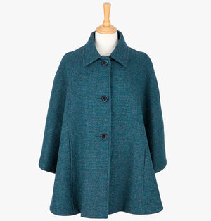 This is the Harris Tweed cape in Teal, the colour is  teal and navy subtle houndstooth check. It has 3 buttons and a collar that can be worn both up and down. It has buttons at the side which hold the cape together to give it more structure. This cape has two pockets and is a one size fits all garment.