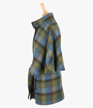 This is the side view of the belted cape in denim sage, the colour is blue, green and brown check. You can see the collar stood up and the sleeves of the cape which come mid-way down the arm. It has two pockets and ties at the waist for a neat silhouette.