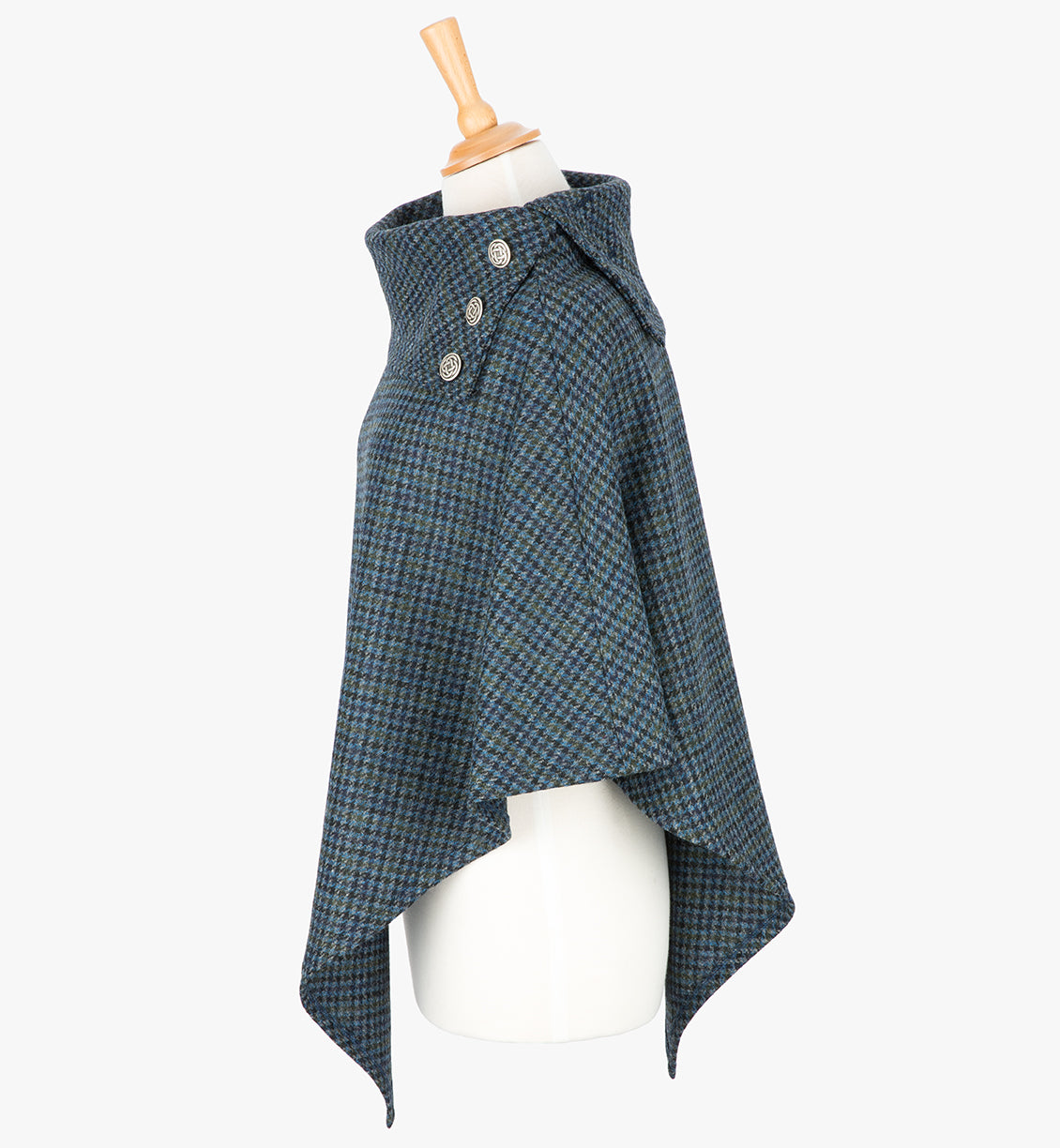 Side view the poncho in mid-blue and black small houndstooth check. It drops over the head and drapes gently over the shoulders. It comes mid-way down the arms and finishes at a point at the front. It has a folded collar with 3 Celtic buttons in silver on the right hand side.