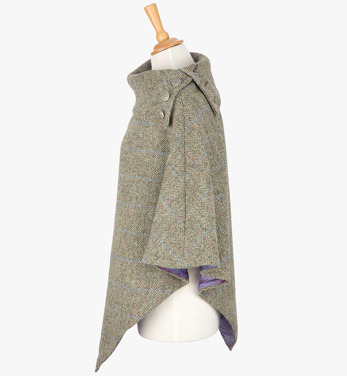 Side view the poncho in pastel check. It drops over the head and drapes gently over the shoulders. It comes mid-way down the arms and finishes at a point at the front. The colour is a neutral brown with a blue and pink overcheck. It has a folded collar with 3 Celtic buttons in silver.