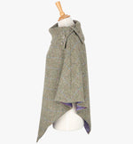 Side view the poncho in pastel check. It drops over the head and drapes gently over the shoulders. It comes mid-way down the arms and finishes at a point at the front. The colour is a neutral brown with a blue and pink overcheck. It has a folded collar with 3 Celtic buttons in silver.