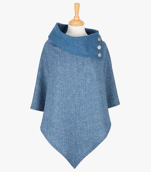 Tweed poncho in sky blue herringbone. It drops over the head and drapes gently over the shoulders. It comes mid-way down the arms and finishes at a point at the front. It has a folded collar in a contrasting sky blue with 3 Celtic buttons in silver on the right hand side.