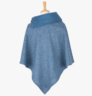 Rear view of the poncho in  sky blue herringbone. It drops over the head and drapes gently over the shoulders. It comes mid-way down the arms and finishes at a point at the back. It has a contrasting folded collar in plain sky blue with 3 button holes on the left.