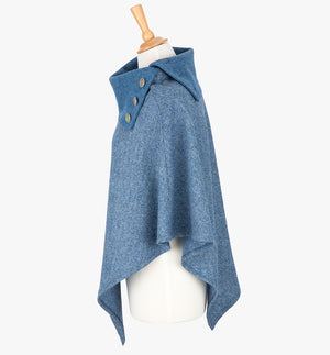 Side view the poncho in sky blue herringbone. It drops over the head and drapes gently over the shoulders. It comes mid-way down the arms and finishes at a point at the front. It has a contrasting folded collar in plain sky blue with 3 Celtic buttons in silver.